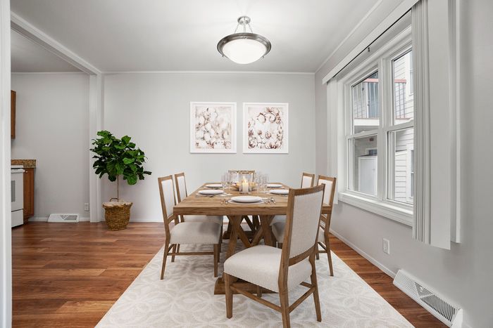 Elegant dining room with a chic wooden table set for six, accented by stylish decor, large window with soft natural light, and warm hardwood flooring.