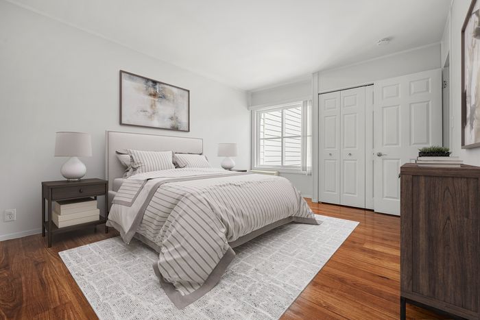Inviting bedroom with cozy bed, elegant nightstands, and natural light from a large window, complemented by warm wooden floors.