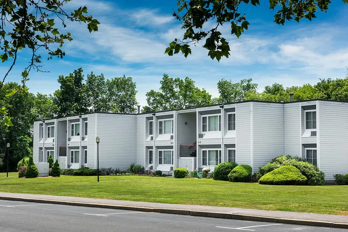 Charming two-story apartment building surrounded by lush greenery and manicured lawns under a bright blue sky.