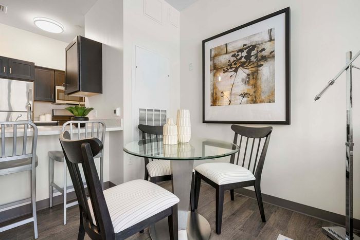 Contemporary dining area with a glass-top table, sleek black chairs, and elegant decor adjacent to a modern kitchen, perfect for cozy gatherings.