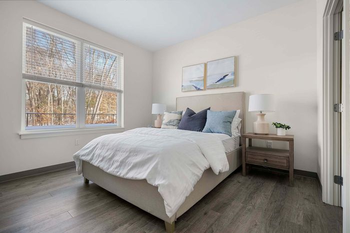 Inviting bedroom featuring a plush bed with cozy pillows, elegant artwork, and a large window with scenic woodland views.