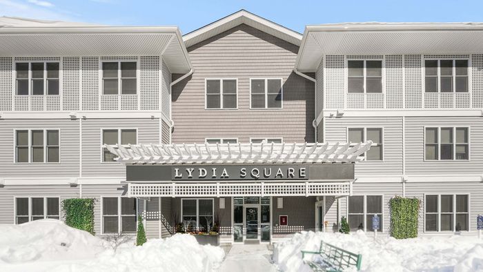Elegant facade of Lydia Square apartment complex with modern architecture, featuring crisp white accents against a snowy backdrop.