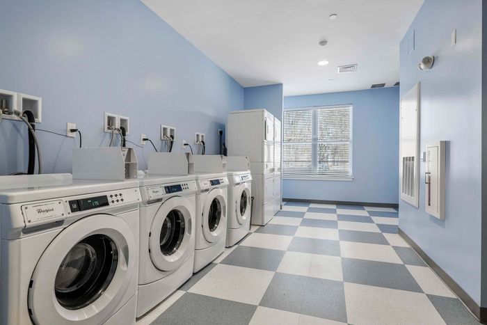 Bright and modern laundry room with multiple washing machines, vibrant blue walls, and checkered tile flooring, creating a fresh and inviting atmosphere.
