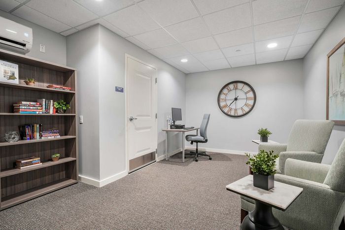 Elegant modern office space with cozy seating, lush greenery, a large decorative clock, and a well-organized bookshelf.