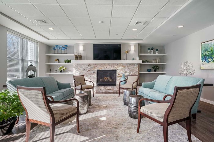 Elegant living room with a modern fireplace, cozy seating, stylish shelving, and abundant natural light.