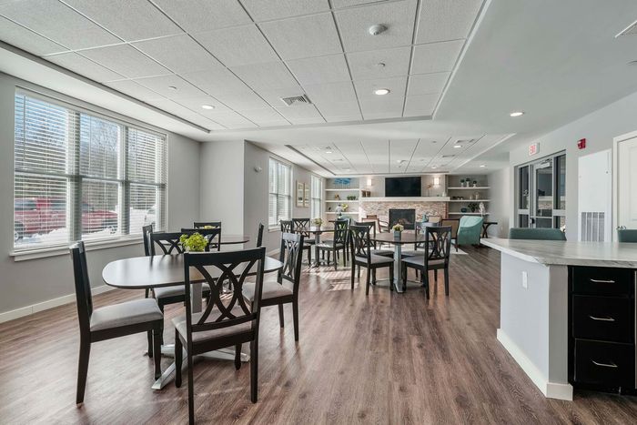 Bright and inviting community room with elegant wooden flooring, modern furnishings, and a cozy fireplace creating a perfect gathering space.