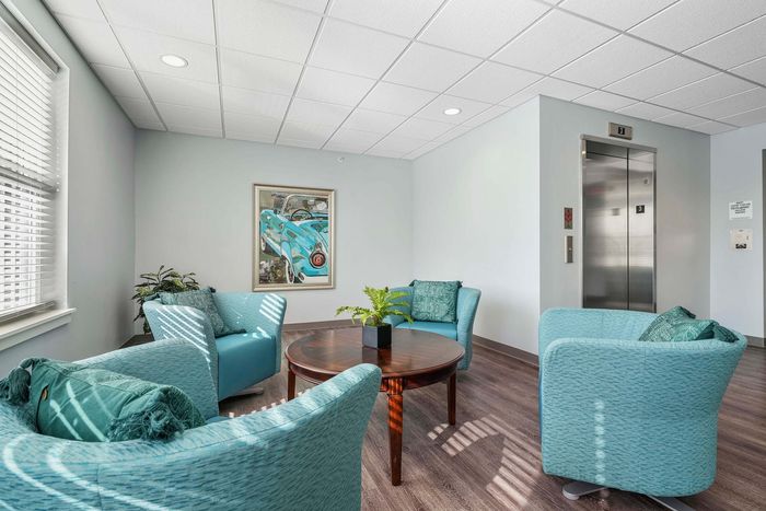 Inviting common area featuring elegant teal armchairs, a chic round table, and modern elevator access, perfect for relaxation and community interaction.