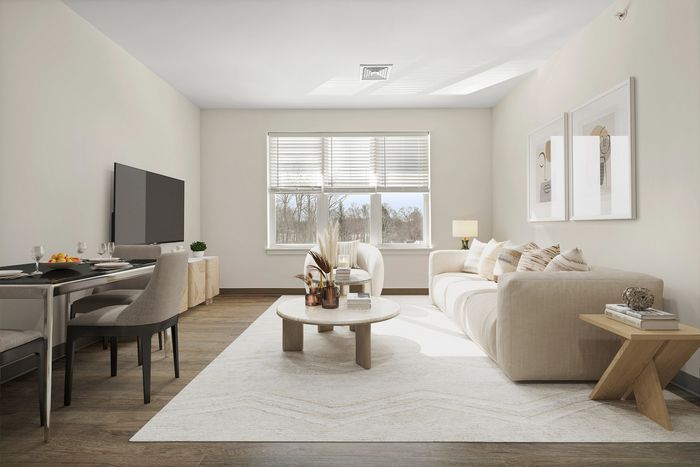 Sunlit living room with chic beige sofa, modern coffee table, large window, wall art, and elegant dining setup.