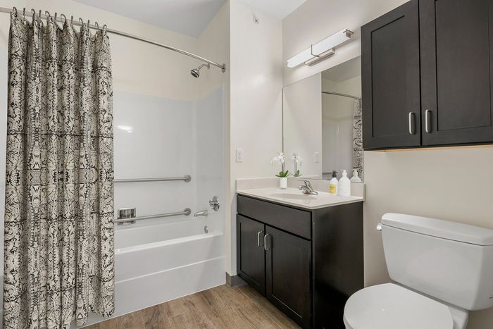 Modern bathroom design featuring elegant cabinetry, sleek countertop with sink, large mirror, and stylish bath and shower combo with a decorative curtain.