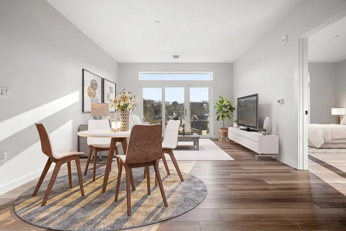 Bright and inviting open-plan living and dining area with elegant decor, hardwood floors, and large windows offering scenic views, next to a cozy bedroom.