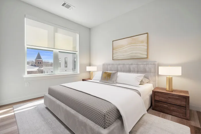 Inviting bedroom with a plush bed, elegant lamps, and a bright window view in a modern apartment.
