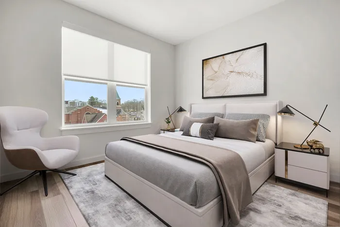 Bright and inviting bedroom with modern decor, featuring a plush bed, chic side table, and a cozy stylish armchair, complemented by a large window offering scenic views.