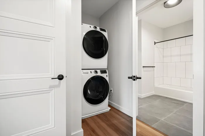 Modern apartment featuring an in-unit stacked washer and dryer set next to a contemporary bathroom with sleek tile flooring and bathtub.