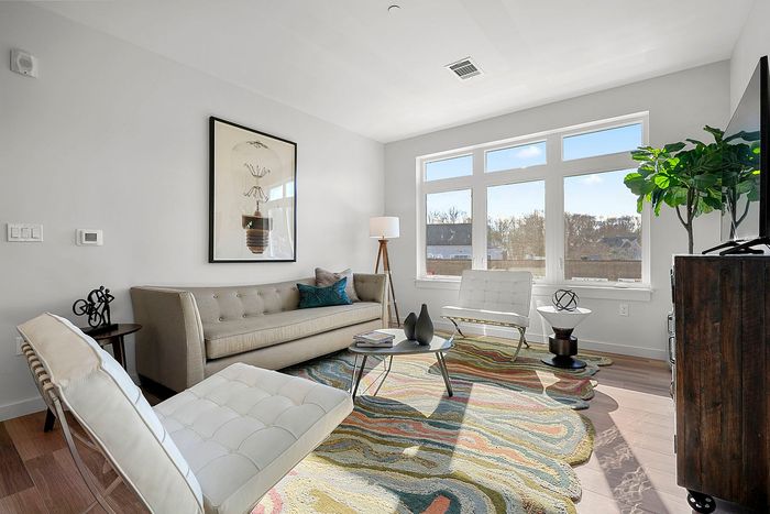 Bright and modern living room with elegant decor, featuring a large window view, contemporary furniture, and a vibrant patterned rug.