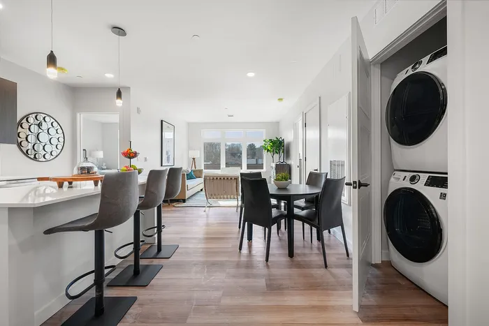 Bright and modern open-plan apartment featuring a stylish kitchen island with bar stools, a cozy dining area, and a spacious living room with large windows.