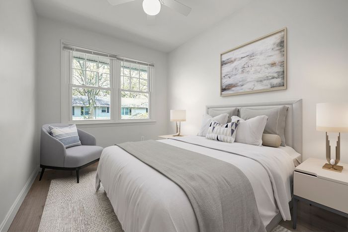 Bright and cozy bedroom with modern decor, featuring a plush bed with elegant pillows, an inviting armchair, and soft natural light through large windows.