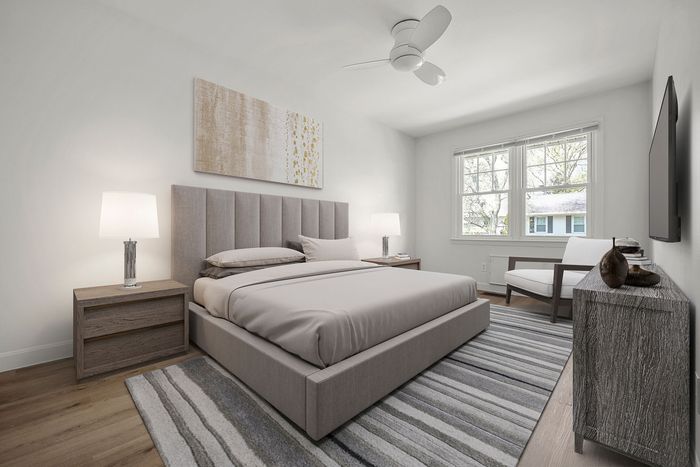 Modern bedroom featuring a chic upholstered bed, elegant nightstands with lamps, and a cozy armchair, bathed in natural light from a large window.