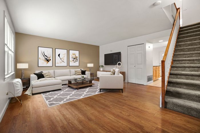 Inviting living room with modern decor, including a spacious sectional sofa, stylish art, and a cozy ambiance, complemented by warm wooden floors and plush carpeted stairs.