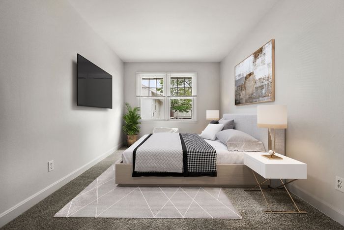 Modern bedroom with a cozy bed, stylish side tables, large flat-screen TV, and a window offering natural light and a view of greenery.