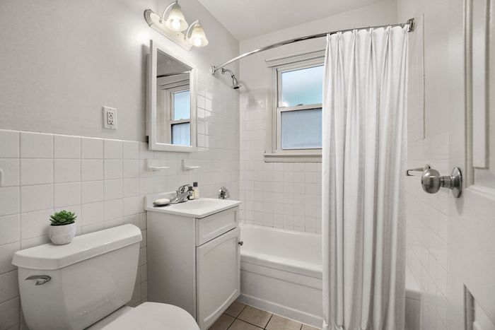 Bright and elegant bathroom with modern fixtures, featuring a sleek white vanity, bathtub, and charming natural light.