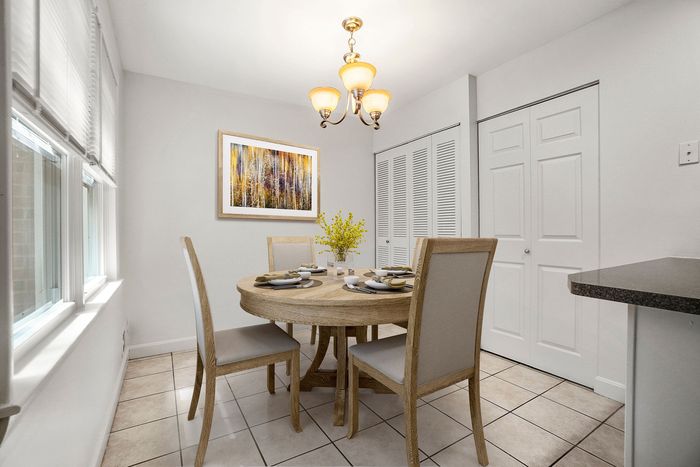 Bright dining area featuring a chic round wooden table set for four, under elegant pendant lighting, complemented by soft natural light from wide windows.