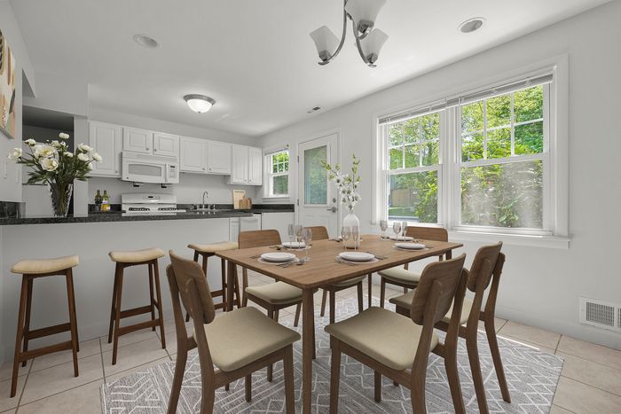 Bright and elegant dining area with a wooden table, modern seating, and a chic kitchen featuring white cabinetry, perfect for hosting gatherings.
