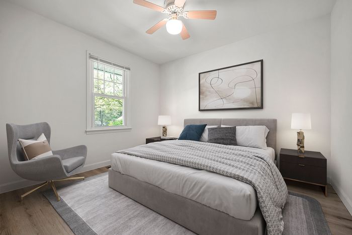 Contemporary bedroom with plush gray bedding, elegant armchair, and modern art. Light-filled space with hardwood floors and stylish decor.