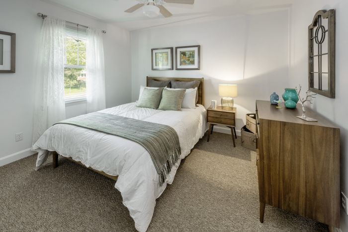 Inviting bedroom with cozy ambiance, featuring a comfortable bed, elegant wooden furniture, and large sunlit window for a serene retreat.