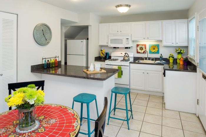 Bright, modern kitchen with white cabinetry, colorful decor, and a cheerful dining area featuring a vibrant, tiled table.