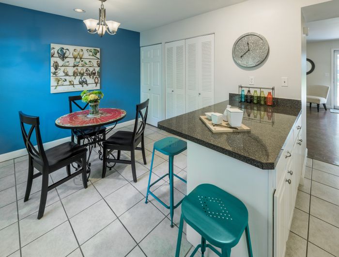 Charming dining area with vibrant blue accent wall, featuring a small round table, elegant black chairs, and a modern breakfast bar with teal stools.