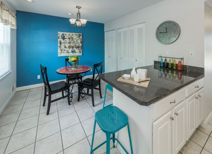 Contemporary dining area with vibrant blue accents, featuring a stylish round table and modern kitchen counter with sleek white cabinetry.