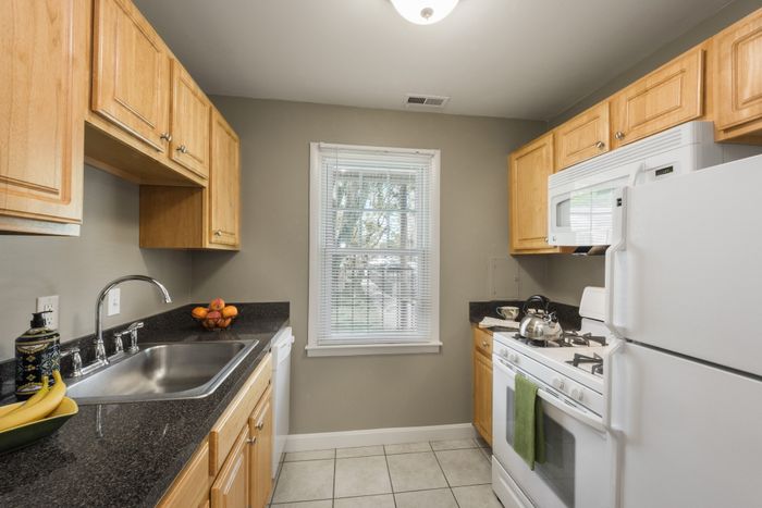 Charming kitchen with wooden cabinets, modern appliances, and a cozy garden view through a bright window.