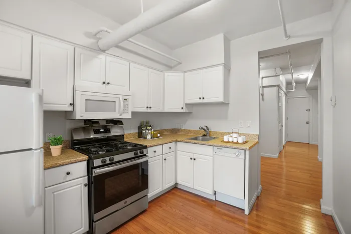 Bright modern kitchen with white cabinetry, stainless steel appliances, and elegant wood flooring.