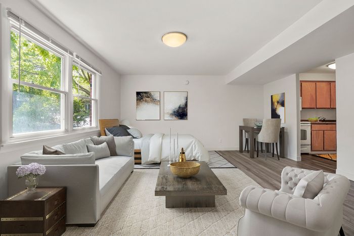 Inviting studio apartment with a cozy living area, stylish decor, large windows offering abundant natural light, and a sleek dining space adjacent to a compact kitchen.