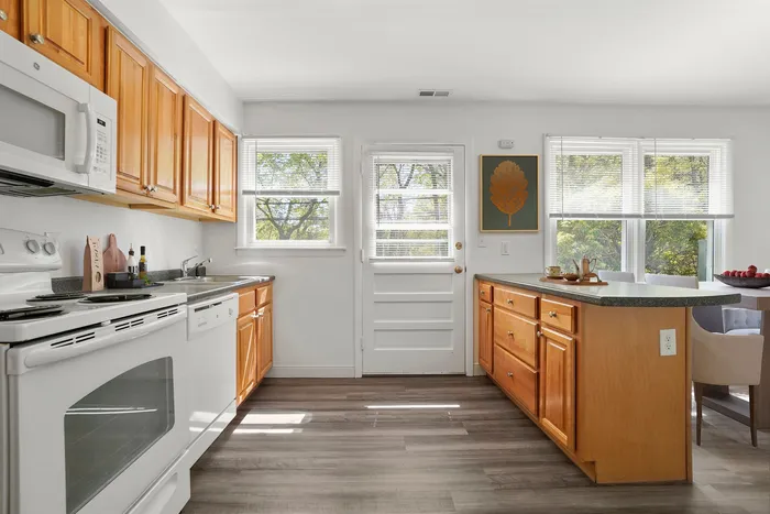 Bright and inviting kitchen with wooden cabinetry, modern appliances, and ample counter space, complemented by large windows letting in natural light.