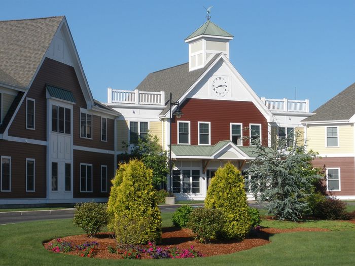 Charming residential complex with New England architecture, featuring a clock tower and vibrant landscaped gardens.