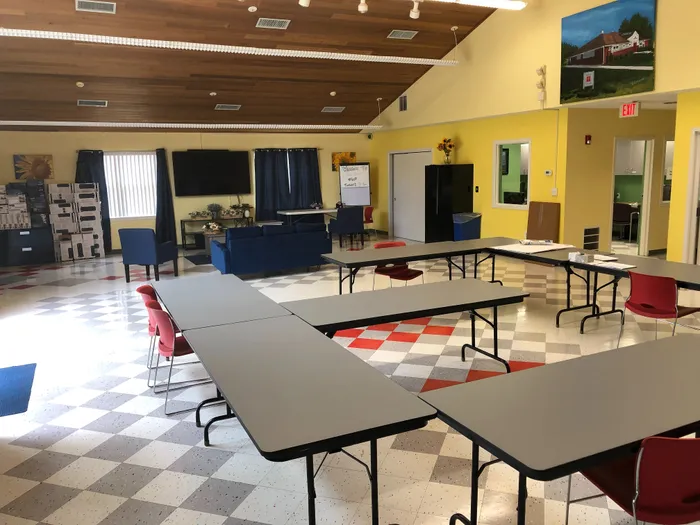 Inviting multipurpose community room with modern furnishings, vibrant yellow walls, and ample natural light; features flexible seating options for events or gatherings.