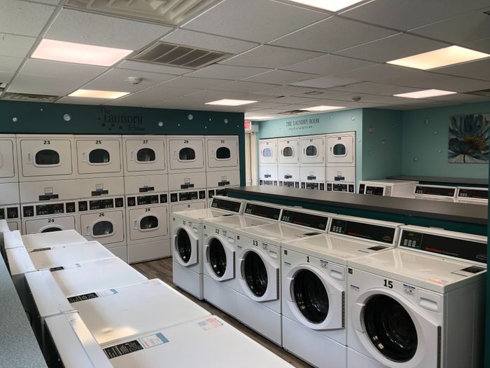 Modern laundry room with multiple washers and dryers, teal accents, and efficient layout.