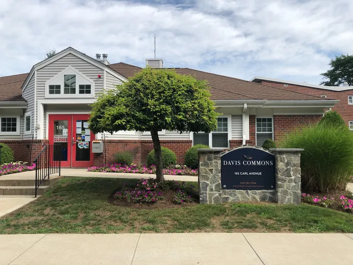 Charming community building of Davis Commons with modern brick facade, vibrant landscaping, and inviting red entrance doors.