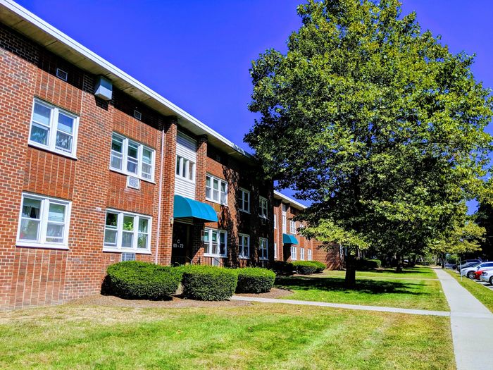 Inviting brick apartment building with lush green lawns and tree-lined sidewalks, perfect for city living.
