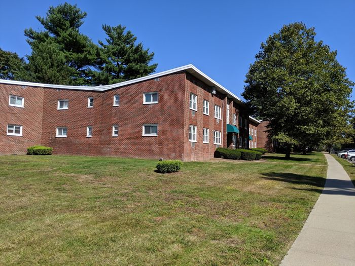 Charming brick apartment building with lush green lawns and mature trees, offering a peaceful and welcoming atmosphere.