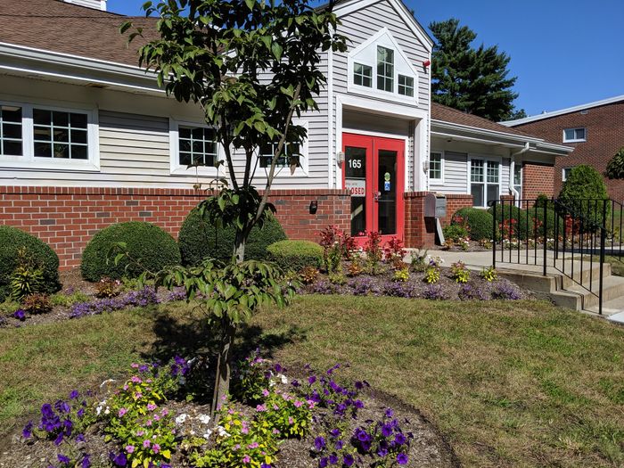 Charming apartment exterior with vibrant flower garden and inviting red door entrance.