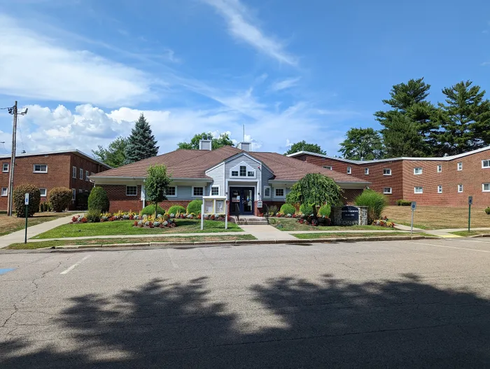 Charming residential complex with lush landscaping, featuring a classic brick facade and inviting entrance under a bright blue sky.