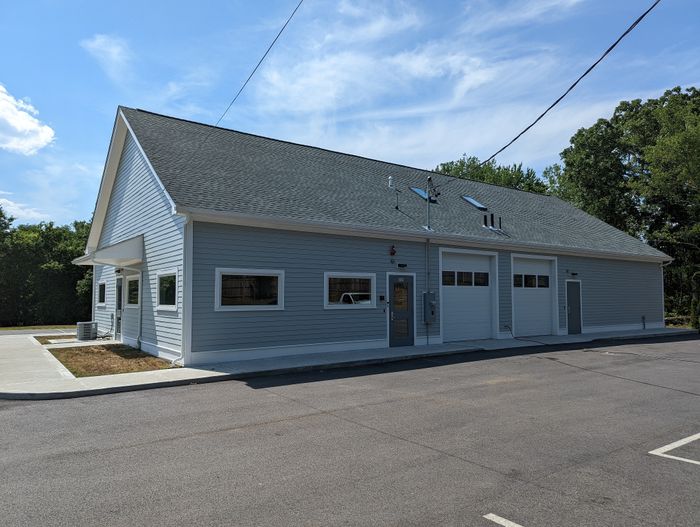 Charming light gray building with a sloped roof, featuring double garage doors and a side entrance, set against a clear blue sky.