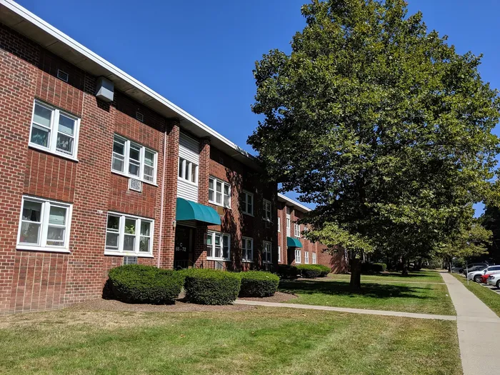 Charming brick apartment building with lush greenery and pleasant sidewalk views.