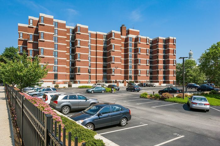 Charming brick apartment building with ample parking and lush greenery, perfect for comfortable urban living.