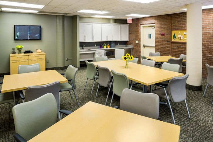 Inviting community room with modern decor, featuring stylish tables, comfortable chairs, cozy lighting, and a well-equipped kitchenette with bright sunflowers for a cheerful touch.
