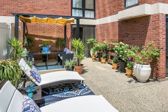 Charming outdoor patio with vibrant potted plants, modern seating area under a stylish pergola, and inviting sun loungers.