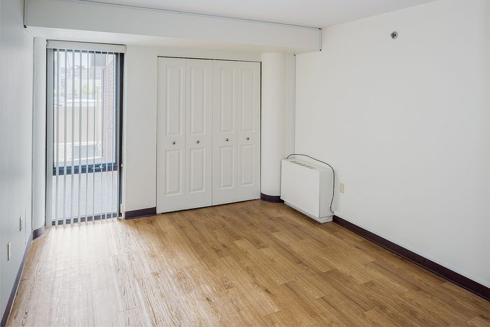 Bright room featuring sleek wood floors, large closet with double doors, and natural light streaming through vertical blinds.