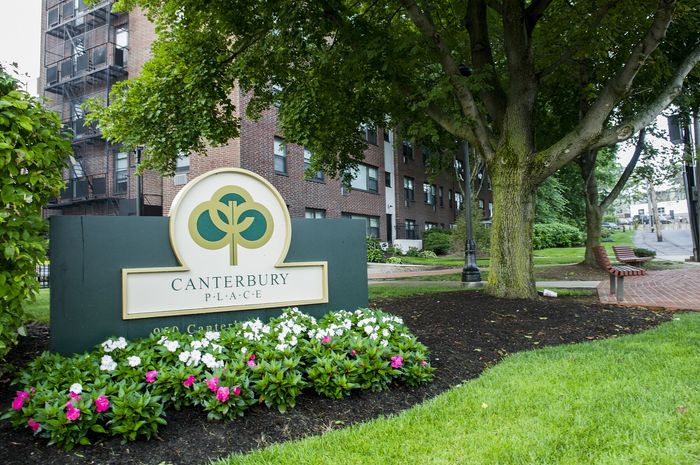 Charming Canterbury Place exterior showcasing lush greenery, blooming flowers, and inviting benches under a canopy of trees.